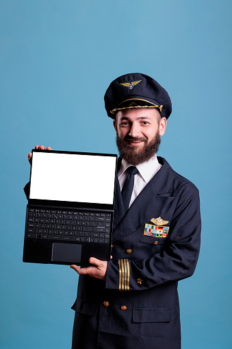 Smiling airliner captain showing laptop with blank white screen, software advertising, pc with website mockup. Plane aviator holding portable computer with empty display for web promotion