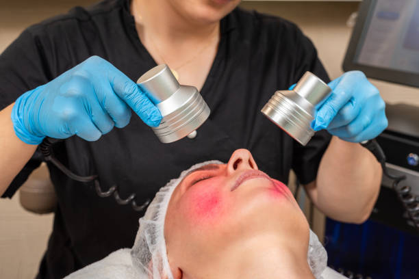Beautician doing skin care with red light therapy stock photo
