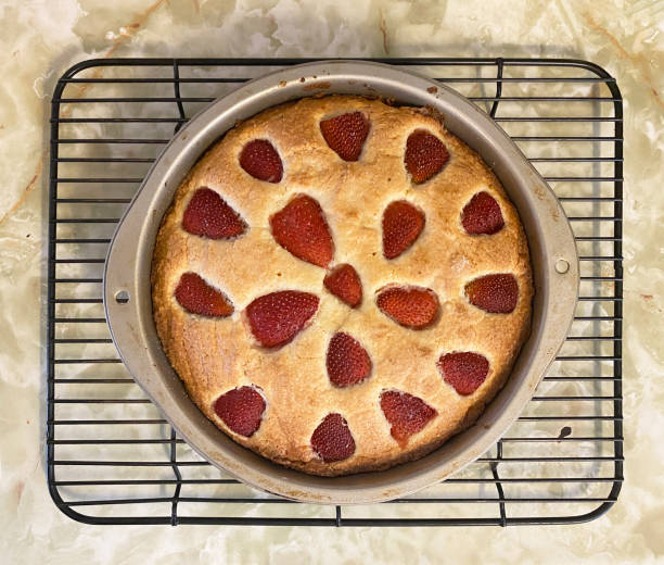 A top angle view of a strawberry cake in a pan on a cooling rack.