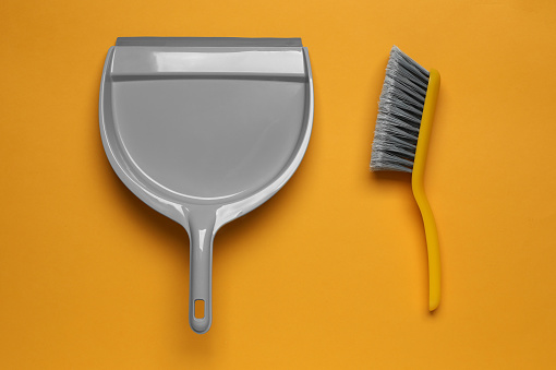 Plastic hand broom and scoop on yellow background, flat lay