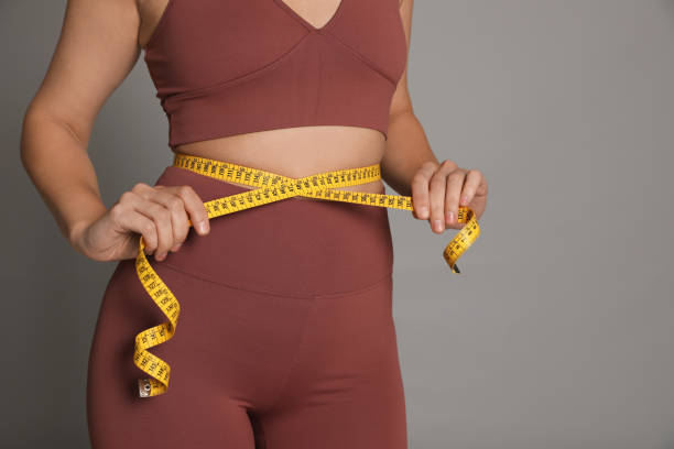 Woman measuring waist with tape on grey background, closeup stock photo