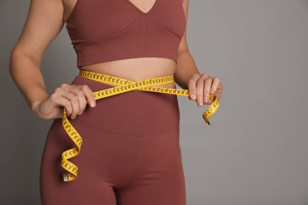 woman measuring waist with tape on grey background, closeup - measuring waist imagens e fotografias de stock