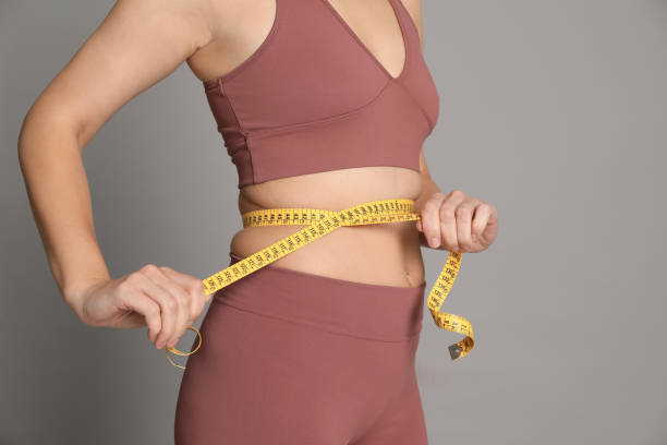 mujer midiendo cintura con cinta sobre fondo gris, primer plano - régimen alimenticio fotografías e imágenes de stock