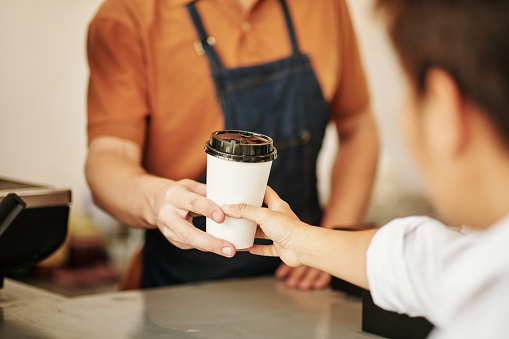 Closeup image of coffeeshop barista giving cup of coffee to customer