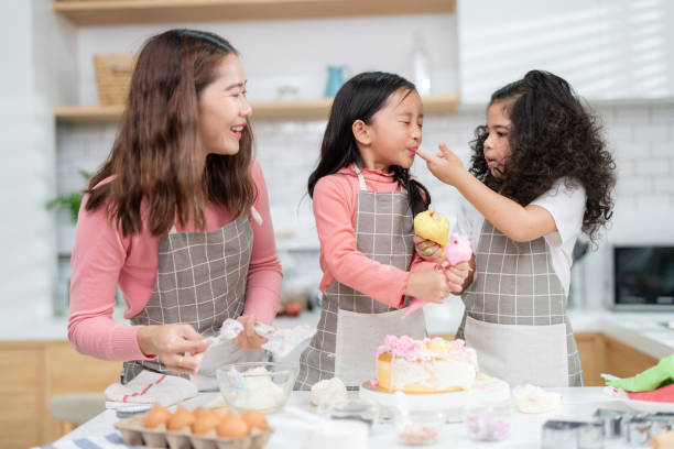 junges kleines mädchen, das in der thekenbäckerei in der modernen küche zu hause steht. viel spaß beim lächeln und genießen am wochenende. zwei kinder in schürze füttern sich gegenseitig mit kuchen. hausgemachtes bäckereikonzept - school classroom child back to school stock-fotos und bilder