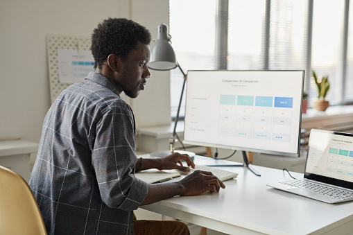 Minimal side view at young black man using computer at workplace in office setting