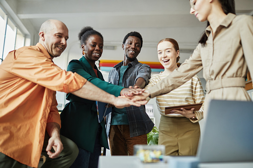 Low angle view at diverse business team huddling in office and stacking hands with motivation