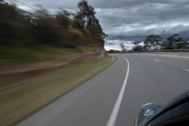 Traveling down a highway at speed approaching a bend. Tree lined highway under a dramatic cloudy sky. Diminishing perspective towards a curve in the road