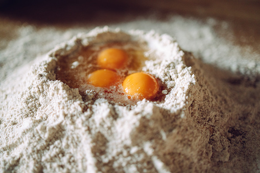 Zoomed photo of the flour pile on the table with three broken eggs in it. No people.