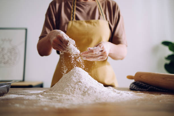 mujer anónima que agrega y prepara harina para amasar - sifting fotografías e imágenes de stock