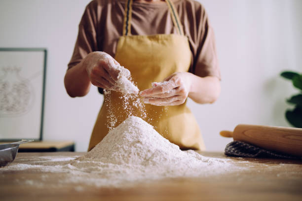 anonymous woman adding and preparing flour for kneading - sifting imagens e fotografias de stock