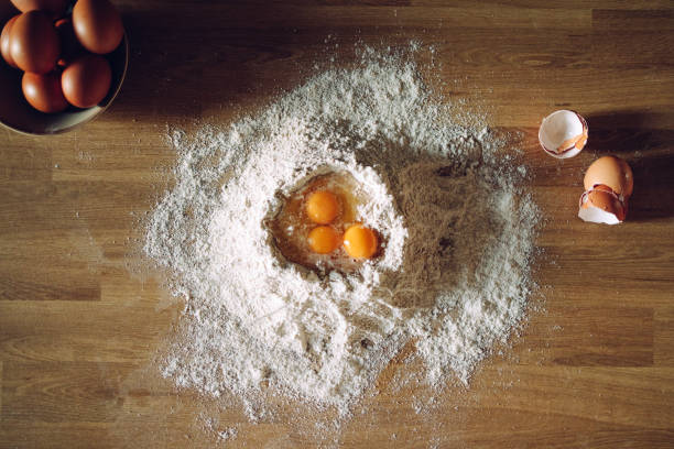 View from above on the flour pile on the table with three broken eggs in it. No people.