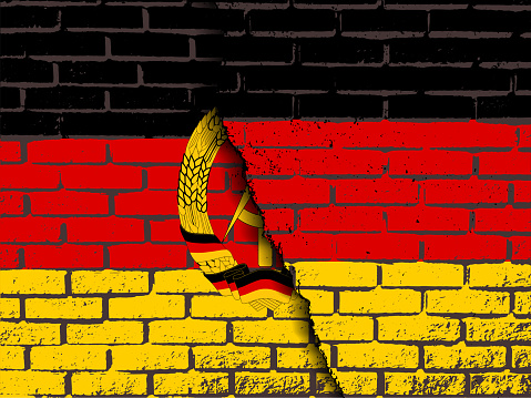 a destroyed brick wall with the flag of Germany on top of the flag of the GDR