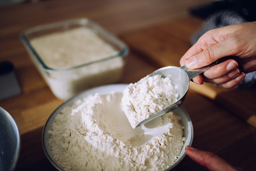 Cropped photo of an anonymous person taking flour from a metal bowl with a flour scoop ready to prepare dough.