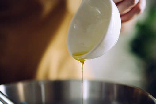 Zoomed in photo of an anonymous woman holding a small white bowl and putting olive oil into the bread dough mixture.
