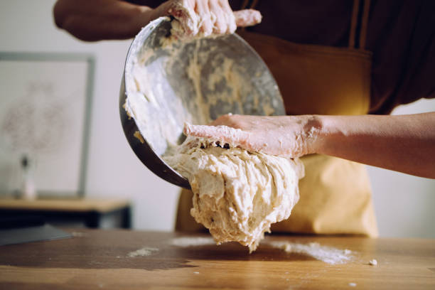 Close up shot of an unrecognizable woman kneading the dough on the work table in her kitchen. She is preparing the homemade bread.