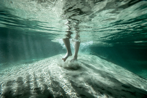 Underwater image of a woman barefoot walking on the sand