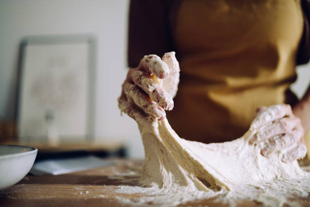 Close up shot of an unrecognizable woman kneading the sticky dough on the work table in her kitchen. She is preparing the homemade bread.