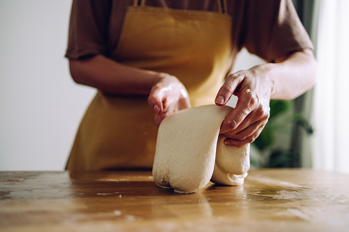 Close up on hands of unknown Caucasian woman making bread. She is kneading the dough on the kitchen counter at home.