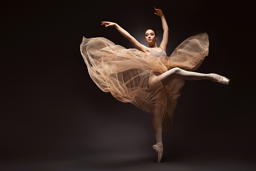 Graceful fly of hands and legs within performing classic dance. Young ballerina dressed in a weightless skirt and ballet pumps is demonstrating dancing skill.  Beauty of classic ballet.