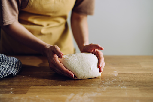 Close up of unrecognizable female baker's hands kneading dough and making bread. She is making a homemade bread and finalizing the dough.