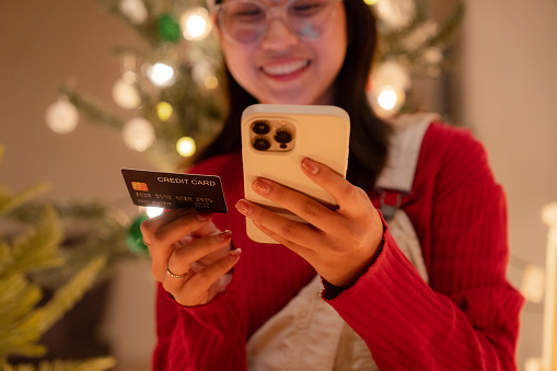 Happy Asian woman making online payment with credit card during shopping Christmas present on e-commerce website.