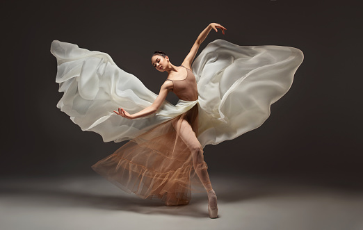 Young graceful ballerina. Elegant woman ballet dancer surrounded by weightless silk cloth and put on in ballet shoes is demonstrating dancing skill. Beauty of classic ballet.