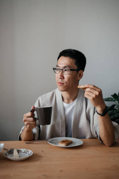 istock Middle aged asian man with spectacles eating breakfast in kitchen. 1421313876