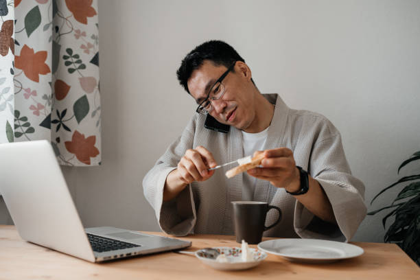 istock Middle aged asian man with smartphone and laptop in kitchen. 1421313881