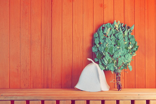 Sauna Accessories on the Shelf. Bath Hat and Birch Broom. Copy Space Photo for Design or Banner. Wooden Bathhouse Background