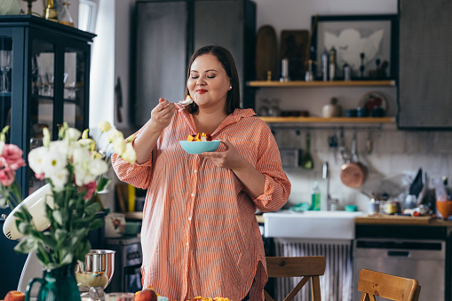 Plus size Caucasian woman enjoying fruit salad with whipped cream in her kitchen.
