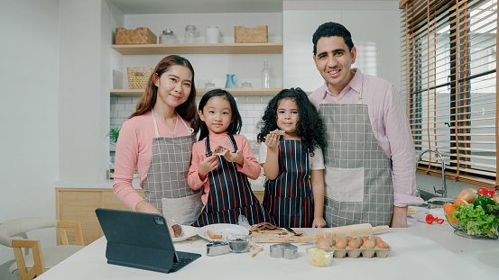 A young father and mother teaching cooking to their two daughters at home during weekend.