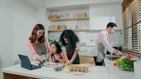 A young girl shaping bread with a star mold while her mother decorates cooked food and her sister observes.