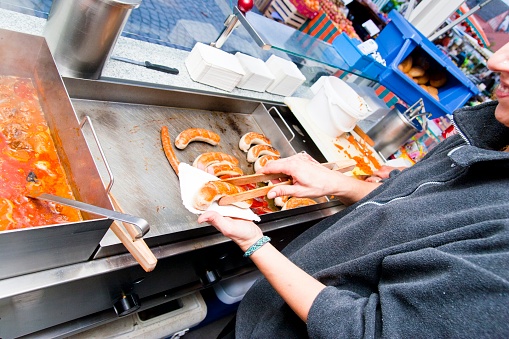 At a food stand, a saleswoman puts a delicious bratwurst fresh from the grill on a cardboard tray.