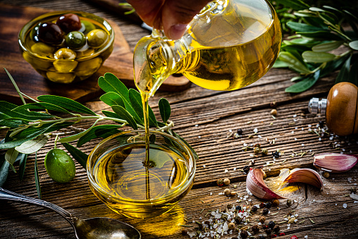 Close up view of  an extra virgin olive oil bottle pouring oil into a glass bowl. Olive tree branches, garlic, salt and peppercorns complete the composition. High resolution 42Mp studio digital capture taken with Sony A7rII and Sony FE 90mm f2.8 macro G OSS lens
