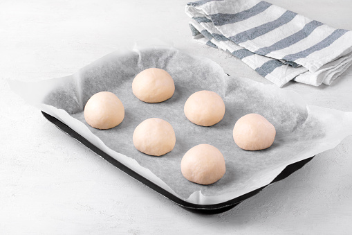 Yeast dough balls on oven tray with parchment. Proofing and preparing to bake buns