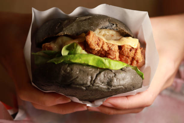 Fast food, people and unhealthy eating concept - close up of woman hands with burger.