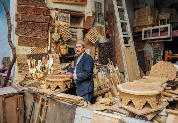 Fez, Morocco - January 07, 2020: Unknown man in his wood working or carving workshop near street market. many wooden souvenirs and products around him