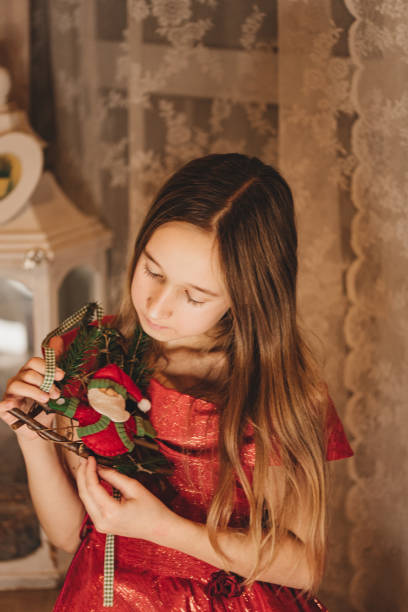 Portrait of a cute little girl with long dark hair in a New Year's red dress. The child decorates the Christmas tree. Holiday and fun concept. Merry Christmas. Christmas tree decorations.