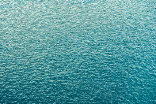 Aerial view of waving sea. Sunlight makes waves reflect white texture.