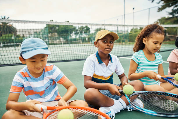 테니스 훈련, 필드 코트 및 야외 스포츠 활동을하는 어린이들. 키즈 팀 휴식, 피트니스 라켓 및 행복한 라이프 스타일. 아시아 어린이, 공을 가진 흑인 소년과 함께 듣는 아프리카 소녀 - tennis court sports training tennis net 뉴스 사진 이미지