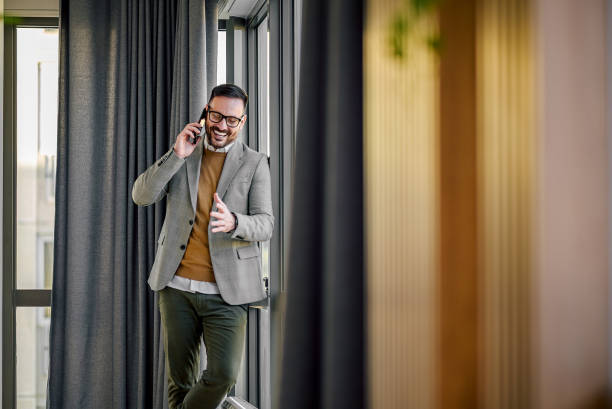 Happy young adult man, telling a joke to his friend over the phone. Excited adult man in a suit, telling something funny to his colleague over the phone, standing in the hall. sales executive stock pictures, royalty-free photos & images
