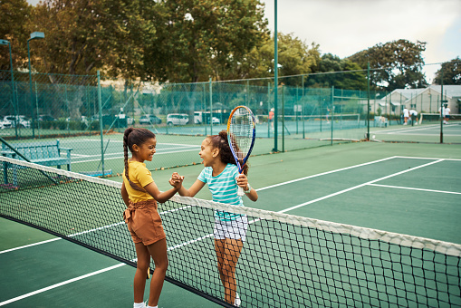 Tennis court, children and friends holding hands at sports net while relaxing together on break. Sporty and happy kids with friendly relationship that has love, trust and support for each other.