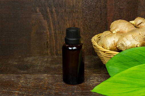 Ginger essential oil in bottle with fresh ginger and green leaf on rustic wooden background. The scientific name is zingiber officinale. Herbs for health care concept.