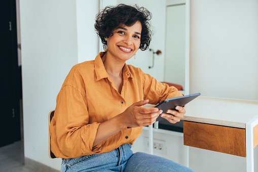 A portrait of a smiling casually dressed Latin-American entrepreneur working online using her tablet.