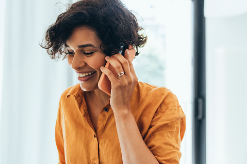 A smiling casually dressed Latin-American entrepreneur calling somebody using her smartphone.