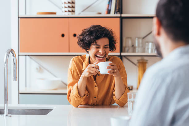 una coppia felice che beve il tè in cucina, parla e ride - tea women cup drinking foto e immagini stock