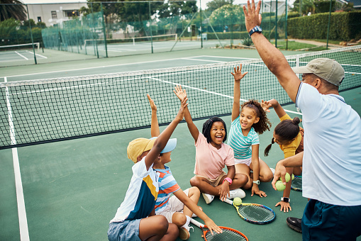 Excited, hands up and tennis lesson for kids on court outside. Coaching, training or learning enthusiastic children doing fitness workout or playing badminton sports with coach outdoors for exercise