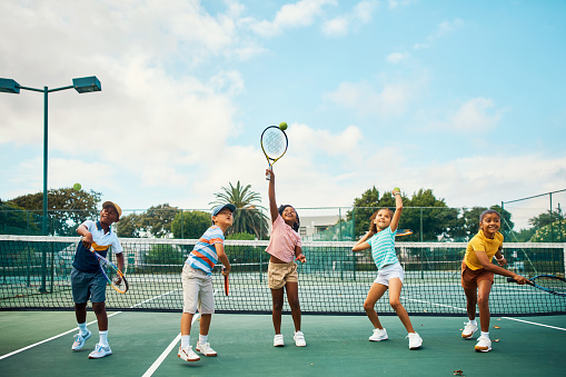 Happy and fun tennis playing children with racket on a court at a sports club. Training, fitness and practice during a lesson with kids learning to play game or sport for health wellness and fitness