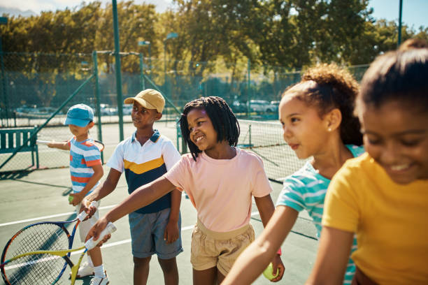 niños aprendiendo tenis en la cancha en clase de educación física en la escuela, estudiantes entrenando para juegos deportivos y haciendo ejercicio físico con deporte para la salud. niños felices y sanos jugando en el partido - tennis child childhood sport fotografías e imágenes de stock